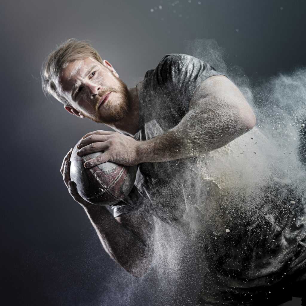 athletic-male-rugby-player-holding-ball-with-dust